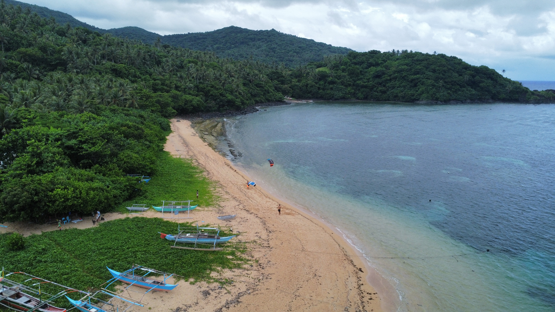 Aerial view of a Philippine beach with bancas and a kite at the shoreline